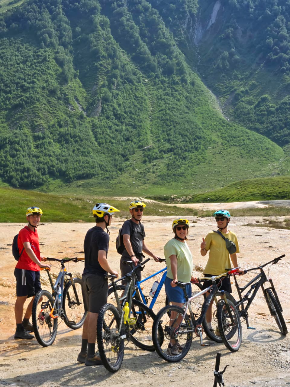 Mountain bikers grouped together in front of lush Caucasus peaks
